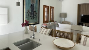 A modern kitchen with a built-in sink, a dining area with a round wooden table, and a living space with a sofa and a television. - VILLA EDENLY ORIENT BAY (saint martin)