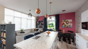 A modern kitchen with a marble countertop, pendant lights, and a dining area with a red table and chairs. - Countryside Escape for Friends and Family (Haslemere)