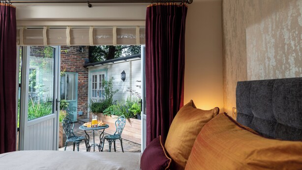 A bedroom with a large bed, a view of a patio with a table and chairs, and a brick wall. - Countryside Escape for Friends and Family (Haslemere)
