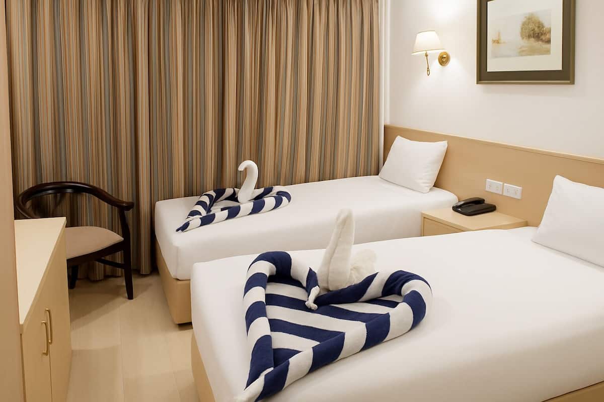 A hotel room with two beds, a desk, a chair, and a lamp.