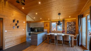 A wooden cabin interior with a kitchen, dining area, and a large window. - Chalet Chanterelle - Cosy and mountainy (Haute-Nendaz)