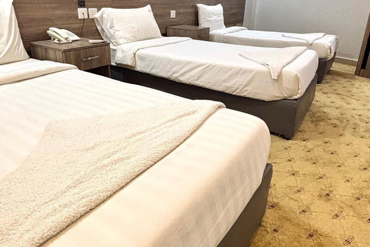 Une chambre d’hôtel avec deux lits, une tête de lit en bois, un téléphone sur la table de chevet et une moquette à motifs.