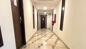 A long, narrow hallway with a checkered floor pattern, doors on both sides, and a fire extinguisher mounted on the wall. - Alabraj Hafawa Hotel Company (Makkah)