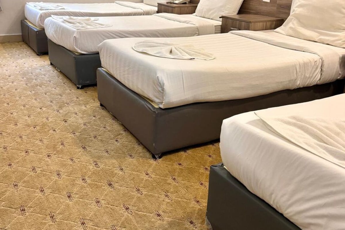 Une chambre d’hôtel avec trois lits alignés, chacun doté d’une tête de lit en bois et d’une literie blanche.