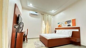 A modern bedroom with a bed, a desk, and an air conditioning unit.