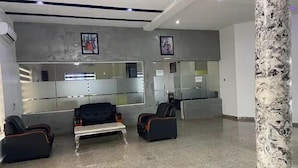 A lobby with a reception desk, seating area with chairs, a marble floor, and a decorative column.
