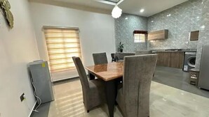 A modern kitchen with a marble backsplash, a dining area with a wooden table and grey upholstered chairs, and a built-in washing machine.