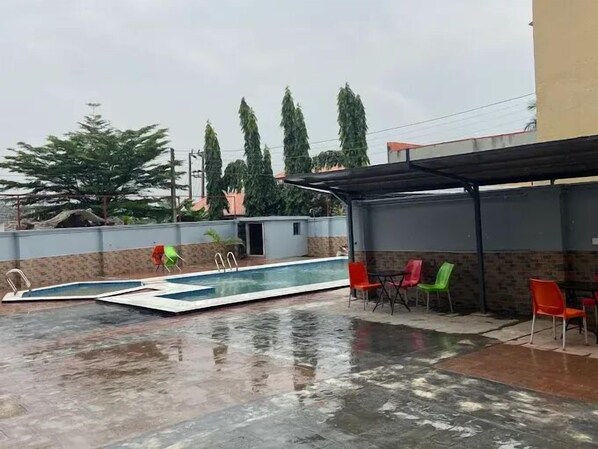 An outdoor swimming pool with a covered seating area and chairs.