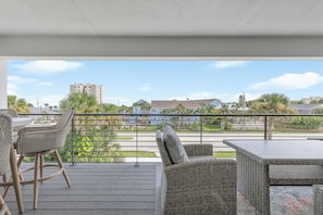 Un espacio al aire libre techado con muebles de mimbre, vista a una zona residencial y cielo despejado.