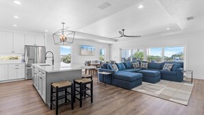 Eine moderne Küche mit einer großen Kochinsel, ein Essbereich mit Blick und ein Wohnzimmer mit Ecksofa.