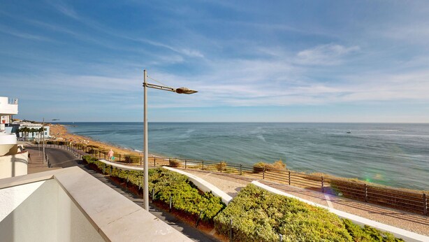 Um calçadão costeiro com vista clara para o mar, um poste de iluminação e um passeio pavimentado.