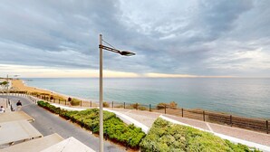 Um calçadão costeiro com um poste de luz de metal, um passeio pavimentado e vista para o mar.