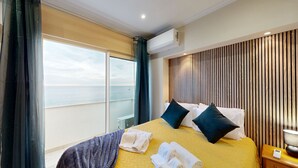 Quarto de hotel com cama, mesa de cabeceira, abajur, janela com cortinas e ar condicionado.