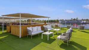 An outdoor deck with a bar area, seating, and a view of a river and a boat.