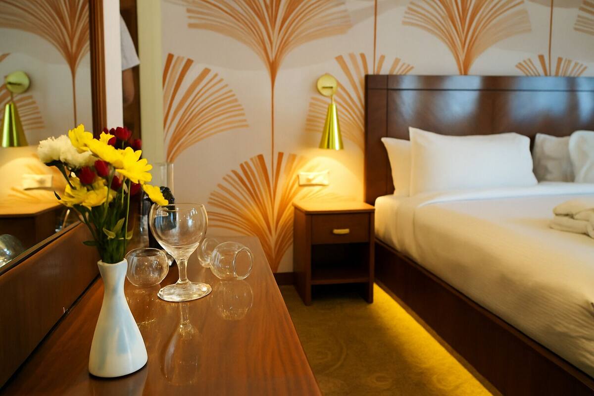 A hotel room with a bed, bedside table, and a vase with flowers.