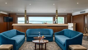 A modern room with a large window, two blue sofas, a small round table, and a wooden bar counter.