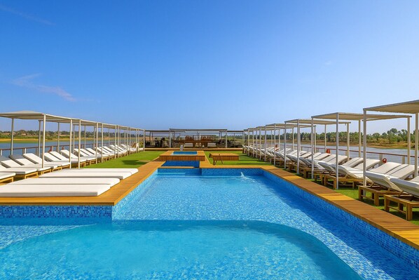 Piscina rectangular con dos carriles, rodeada de sillones de descanso y una cubierta de madera.