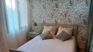 Ein Schlafzimmer mit einem Bett, einem Nachttisch, einer Lampe und einem Fenster mit Vorhängen.
