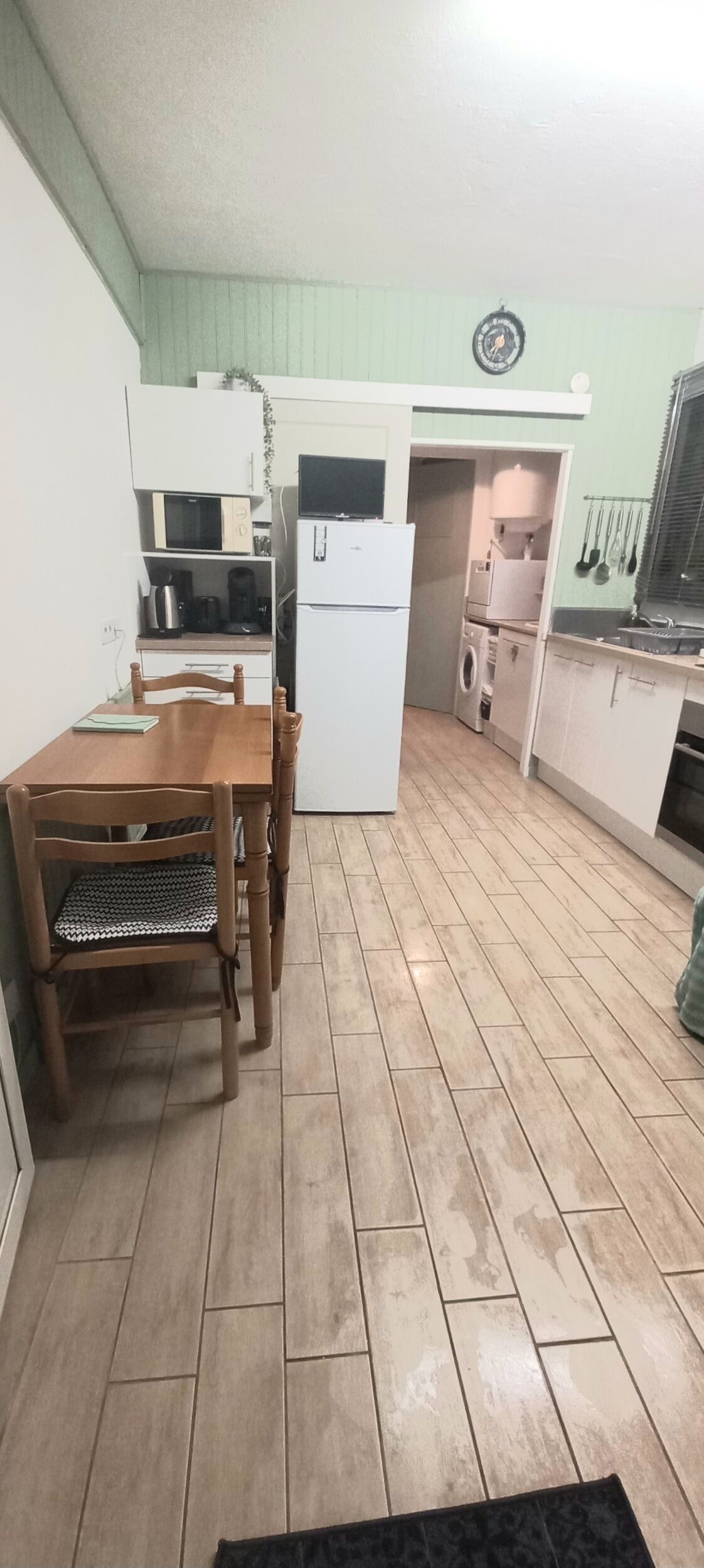 Een kleine keuken met een eettafel en stoelen, een magnetron, een koelkast en een wasmachine.