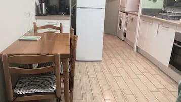 Een kleine keuken met een eettafel en stoelen, een magnetron, een koelkast en een wasmachine.