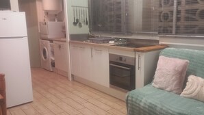 Eine kompakte Küche mit Waschmaschine, Backofen und einer kleinen Essecke mit einer Couch.