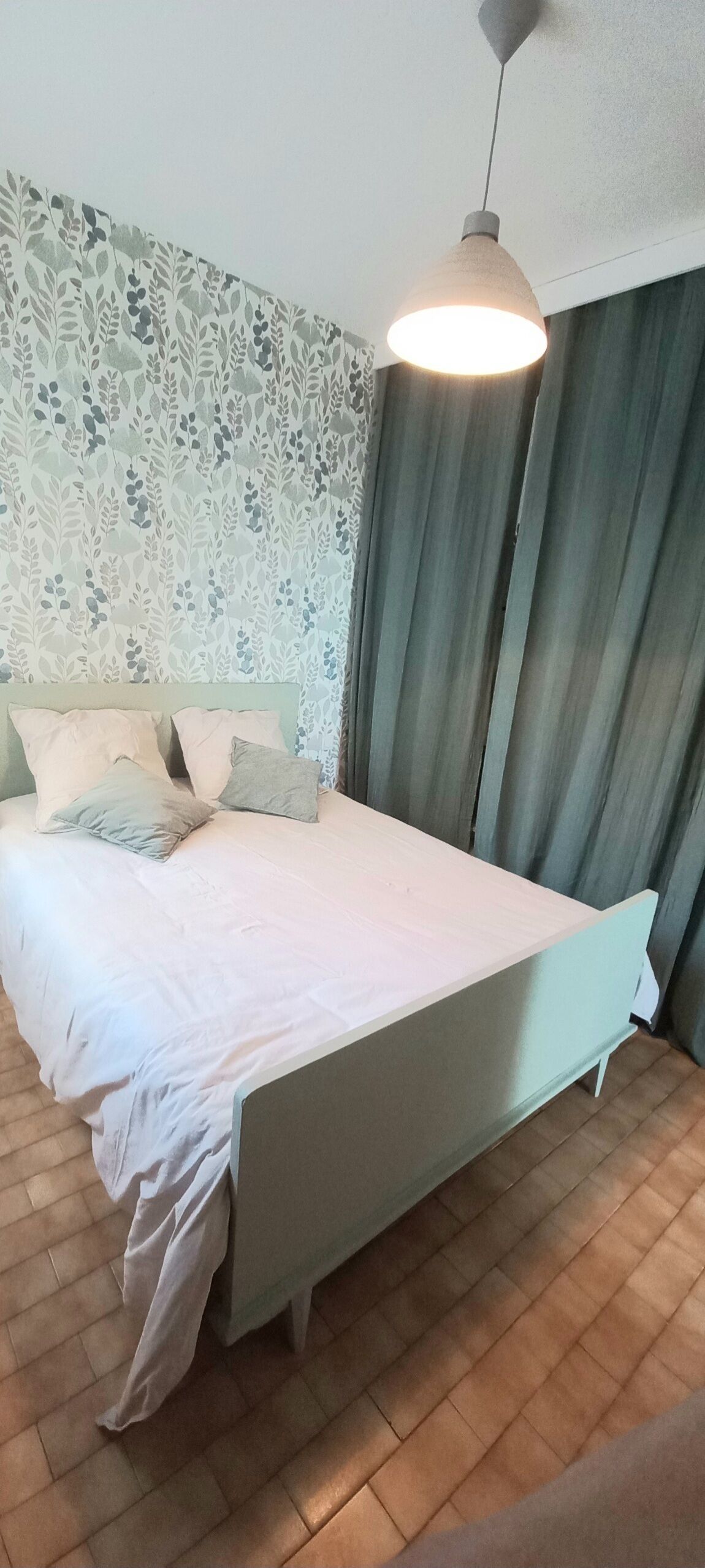 Ein ordentlich bezogenes Bett mit Kissen, eine Pendelleuchte und eine Wand mit Muster.