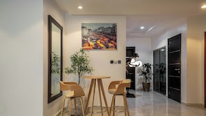 A modern interior with a round table and two wooden chairs, a large framed picture on the wall, and a potted plant.