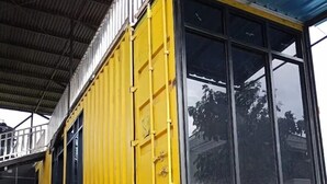 A yellow shipping container converted into a building with large windows, a metal staircase, and a wooden fence in the foreground. - Ijen Menjangan View (Banyuwangi)