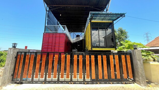 A house with a unique design, featuring a large container as the main structure, a metal roof, and a wooden fence in front. - Ijen Menjangan View (Banyuwangi)