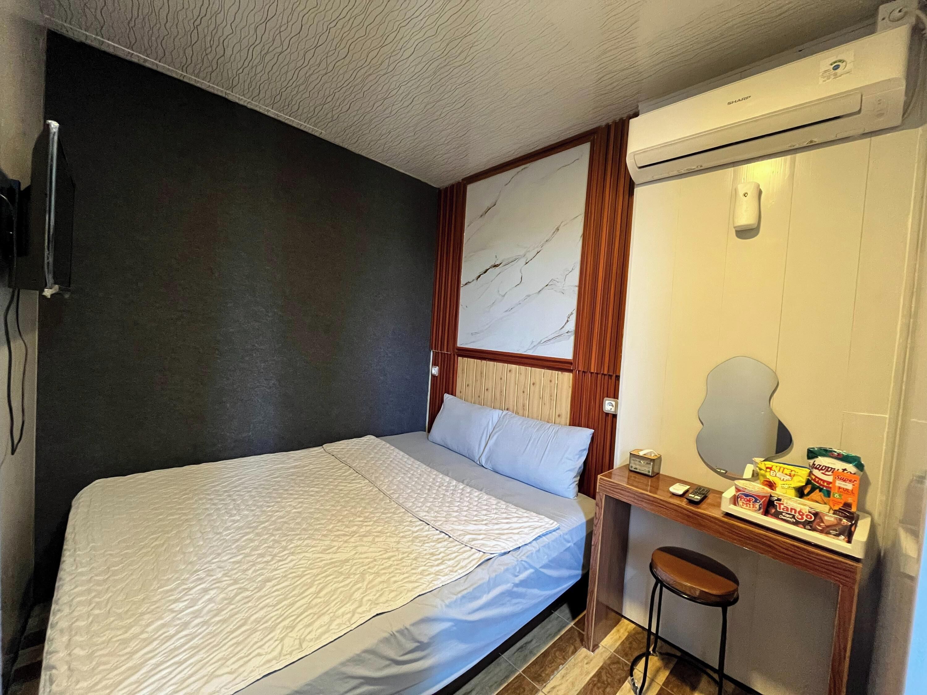 Quarto com cama, escrivaninha, cadeira, espelho e ar condicionado fixado na parede.