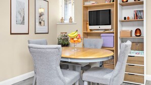 A dining area with a round table, grey upholstered chairs, a fruit bowl, a bookshelf, and a television. - Countryside Retreat on Surrey/Hampshire Border (Haslemere)