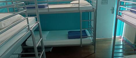 Une chambre de dortoir avec des lits superposés, une fenêtre et une porte sur laquelle est apposée une pancarte.