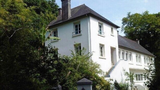 A two-story white building with a dark roof, surrounded by greenery. - Gite D'étape port de Carhaix (Carhaix-Plouguer)