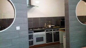A modern kitchen with grey tiles, a gas stove, oven, and a microwave. There are cabinets with handles and a glass range hood. - Gite D'étape port de Carhaix (Carhaix-Plouguer)