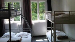 A dormitory room with bunk beds, a window with curtains, and a view of greenery outside. - Gite D'étape port de Carhaix (Carhaix-Plouguer)