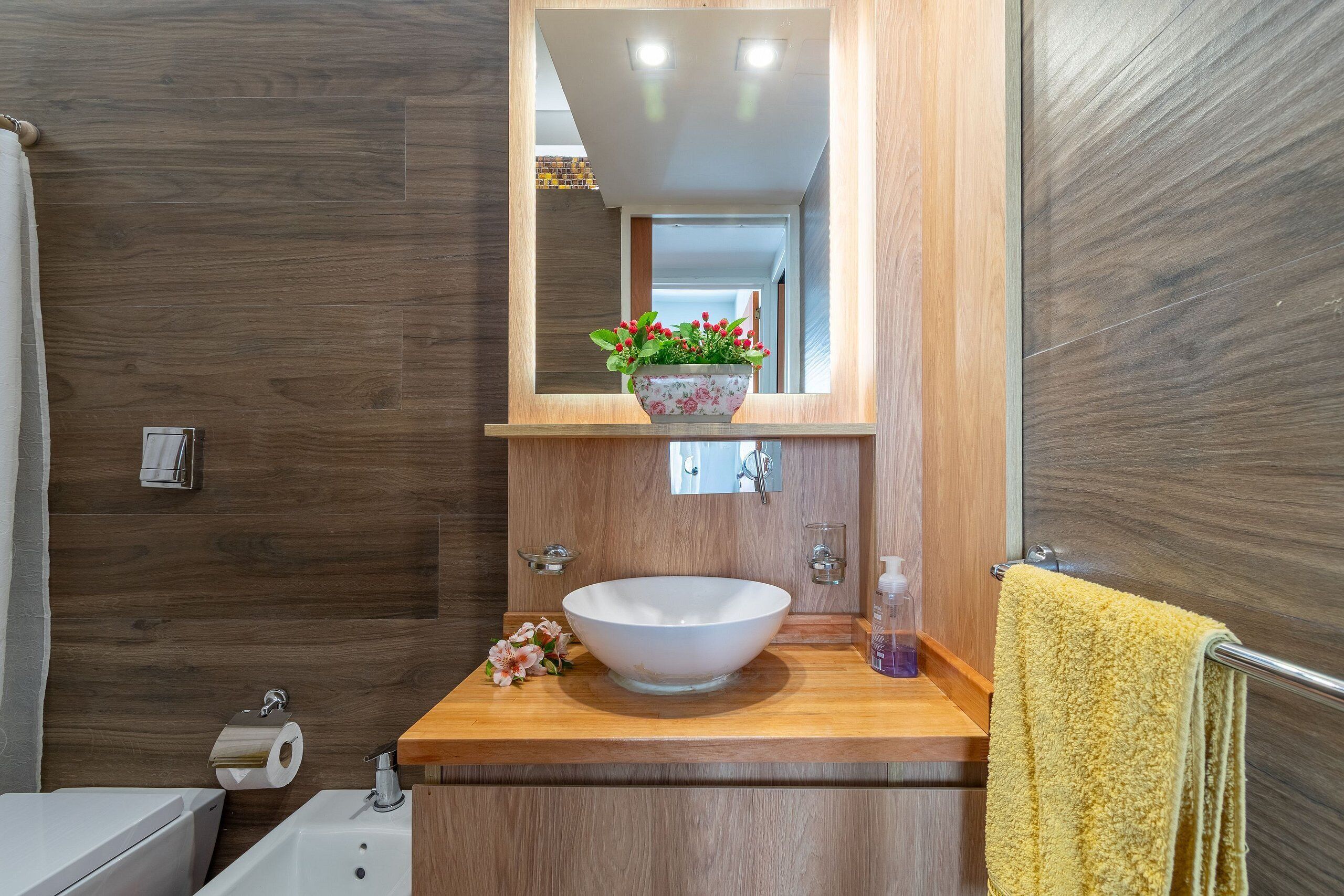 Un baño con un tocador de madera, un lavabo blanco, un espejo y una toalla amarilla.
