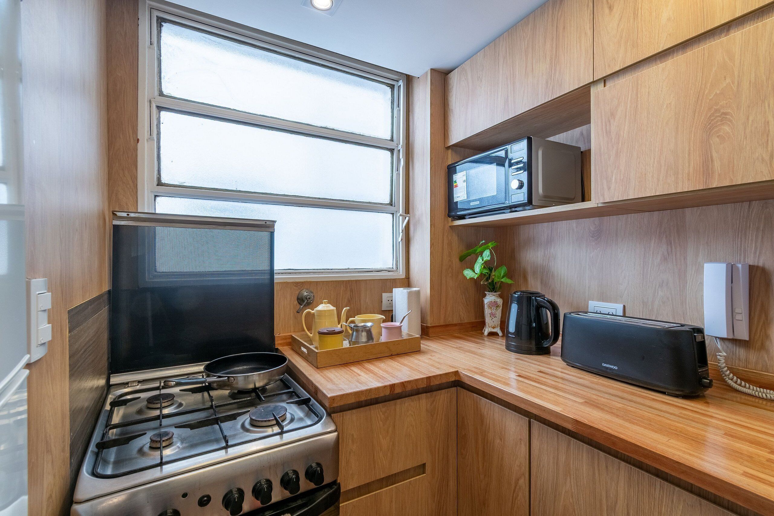 Una cucina compatta con piano cottura a gas, forno a microonde, tostapane e mobili in legno.