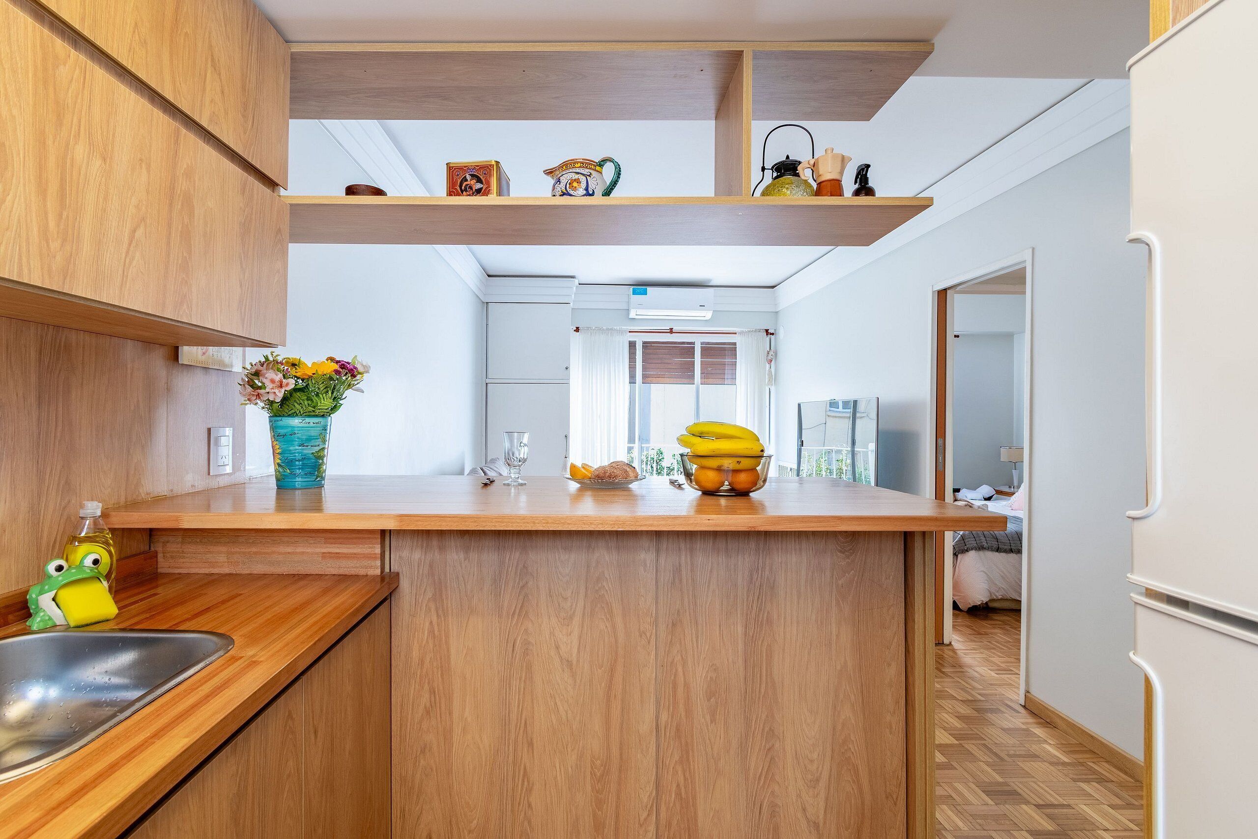 A modern kitchen with wooden cabinets, a wooden countertop, and a built-in island. There is a window with curtains, a sink, and a refrigerator.