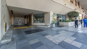 A modern hotel entrance with a glass facade, a concrete exterior, and a small garden area.