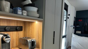 A compact kitchenette with a coffee maker, toaster, and a wooden shelf above.