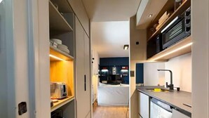 A narrow hallway leading to a compact kitchen with a toaster, a sink, and a microwave.