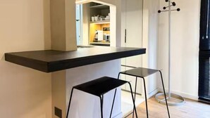 A modern kitchen with a black countertop, two black stools, and a view into the adjacent dining area.