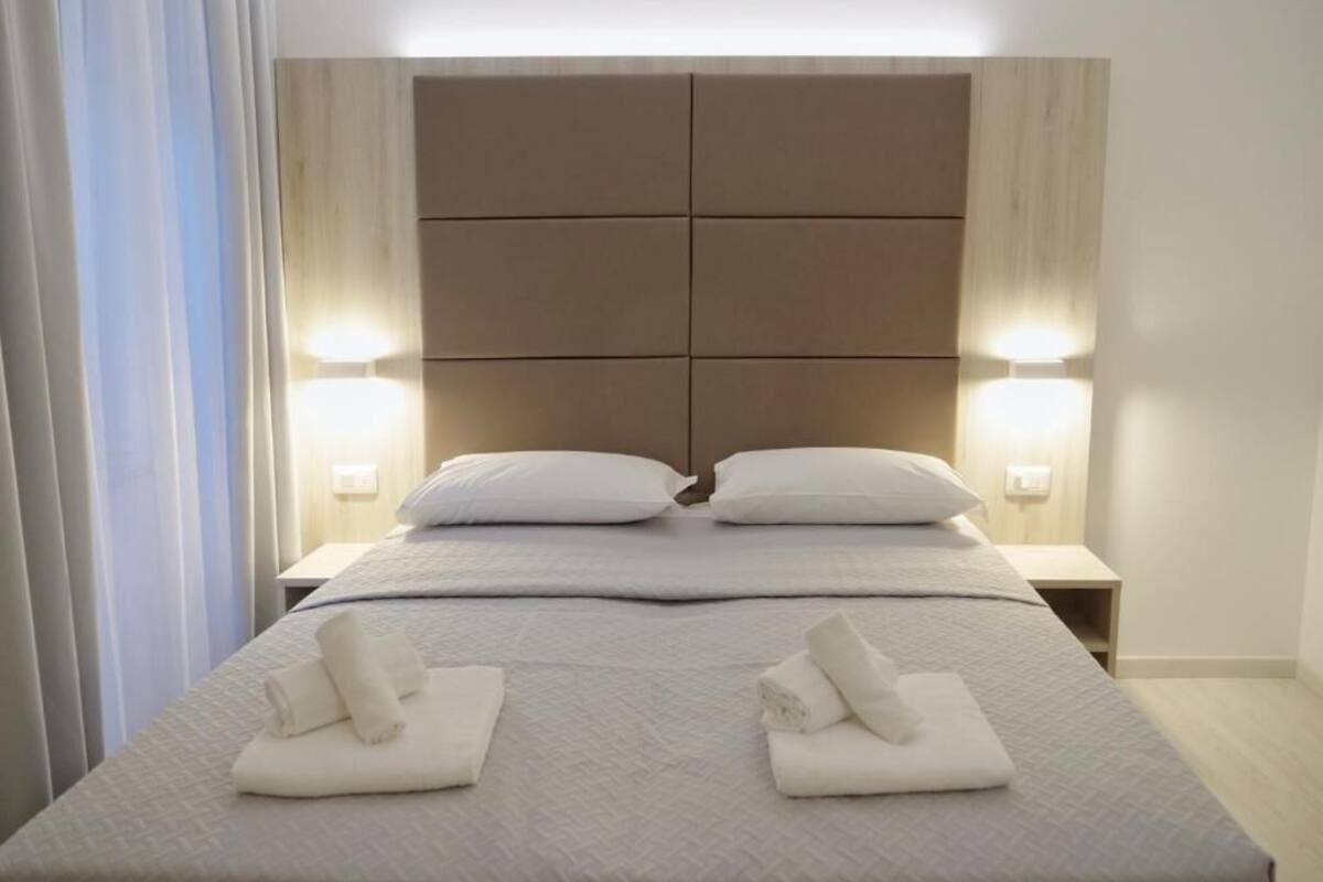 A hotel room with a large bed, two bedside lamps, and neatly folded towels on the bed.