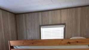 Una cama litera con una ventana encima, paredes de madera y suelo de madera.