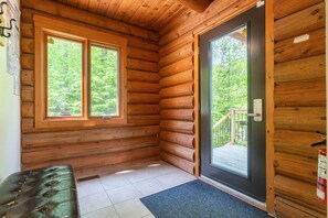 A log cabin room with two windows, a bench, a door, and a fire extinguisher.