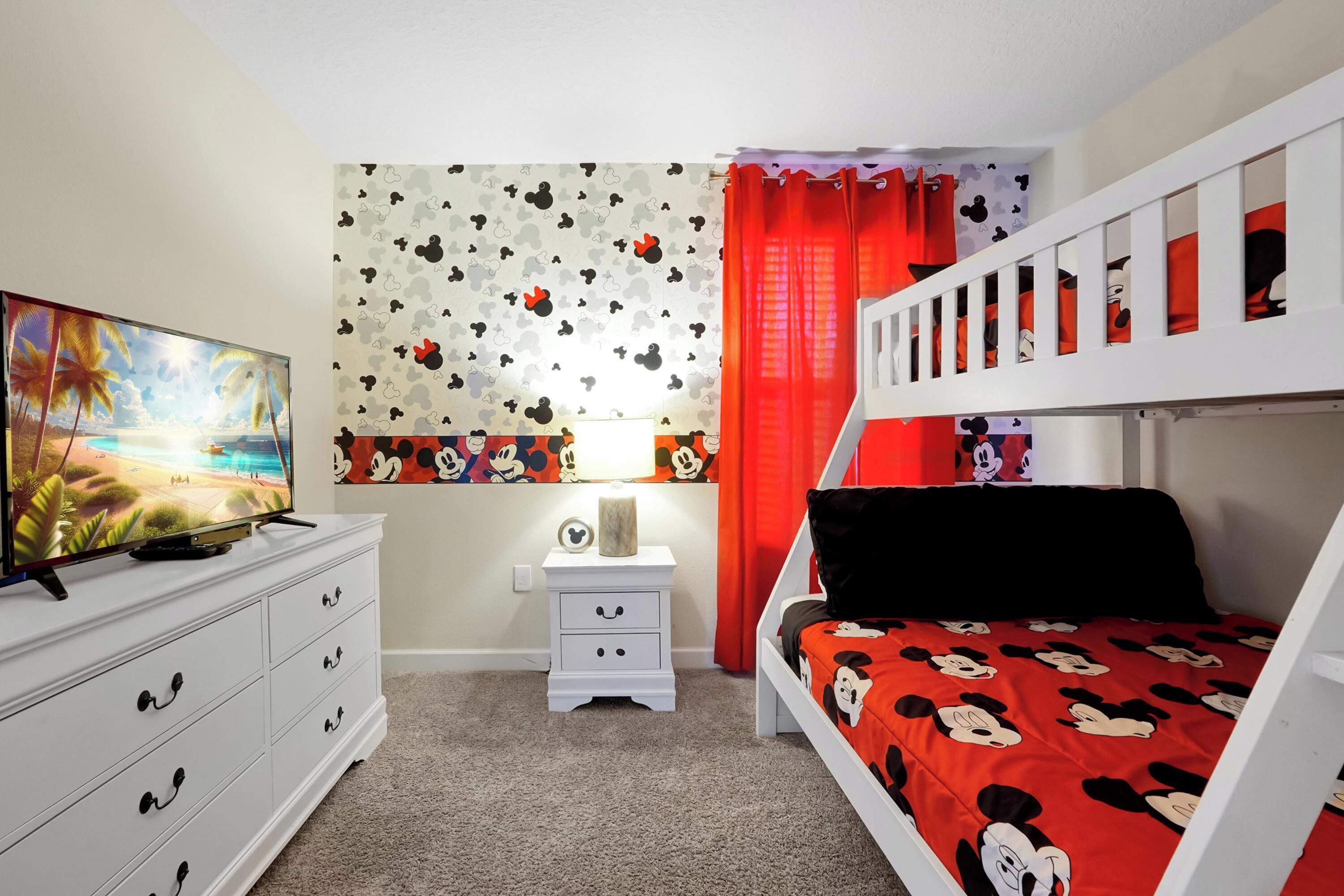 A child's bedroom with a bunk bed, a TV, a dresser, and Mickey Mouse themed wallpaper.