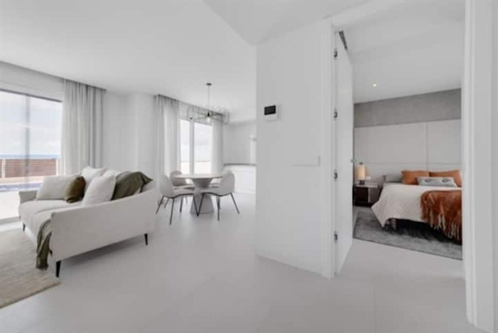 A modern hotel room with a white sofa, a dining table, and a bed with a grey headboard.