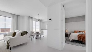 Une chambre d’hôtel moderne avec un canapé blanc, une table à manger et un lit doté d’une tête de lit grise.