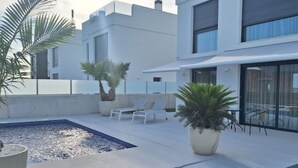 Un patio extérieur moderne doté d’une piscine rectangulaire, de chaises longues et de plantes en pot.