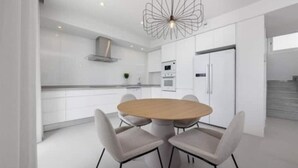 Une cuisine moderne avec des meubles blancs, une table ronde en bois et quatre chaises.